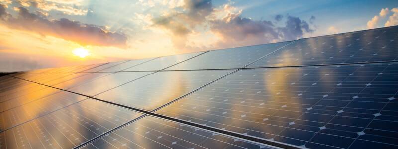 Eine Reihe von Solarpaneelen reflektiert die untergehende Sonne und den teils bewölkten Himmel.