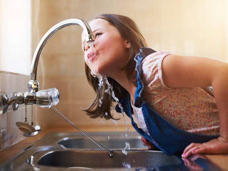 Ein Kind trinkt Wasser direkt aus einem Wasserhahn über einem Spülbecken.