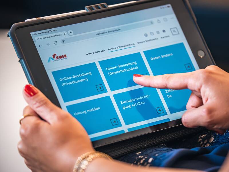 Eine Person bedient ein Tablet mit einer geöffneten Website, die verschiedene Online-Dienstleistungsoptionen anzeigt.