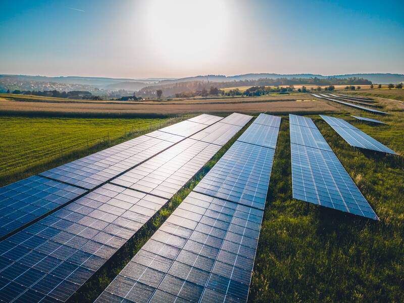 Das Bild zeigt eine weitläufige Solaranlage auf einem Feld unter einem sonnigen Himmel.